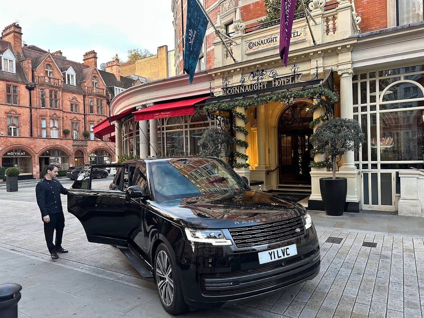 Driver opening the door of a luxury SUV for a business client in Canary Wharf, London
