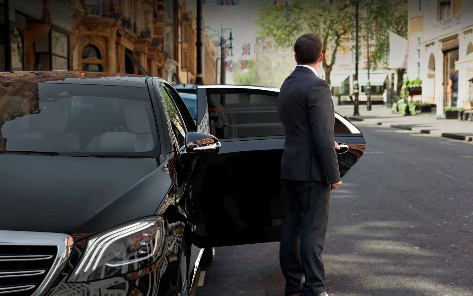 Professional chauffeur standing next to luxury car, waiting to welcome VIP guest in London