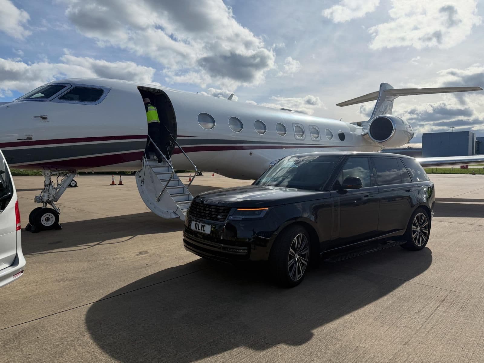 Luxury SUV parked beside a private jet at Farnborough Airport, collecting arriving clients on the tarmac.